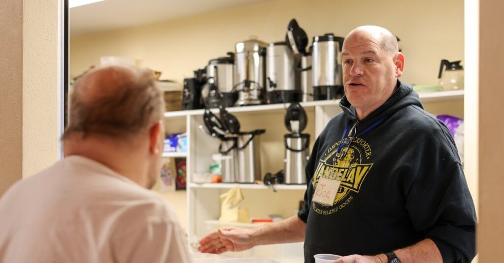 Outreach worker speaking with a participant in a room with coffee urns and supplies.